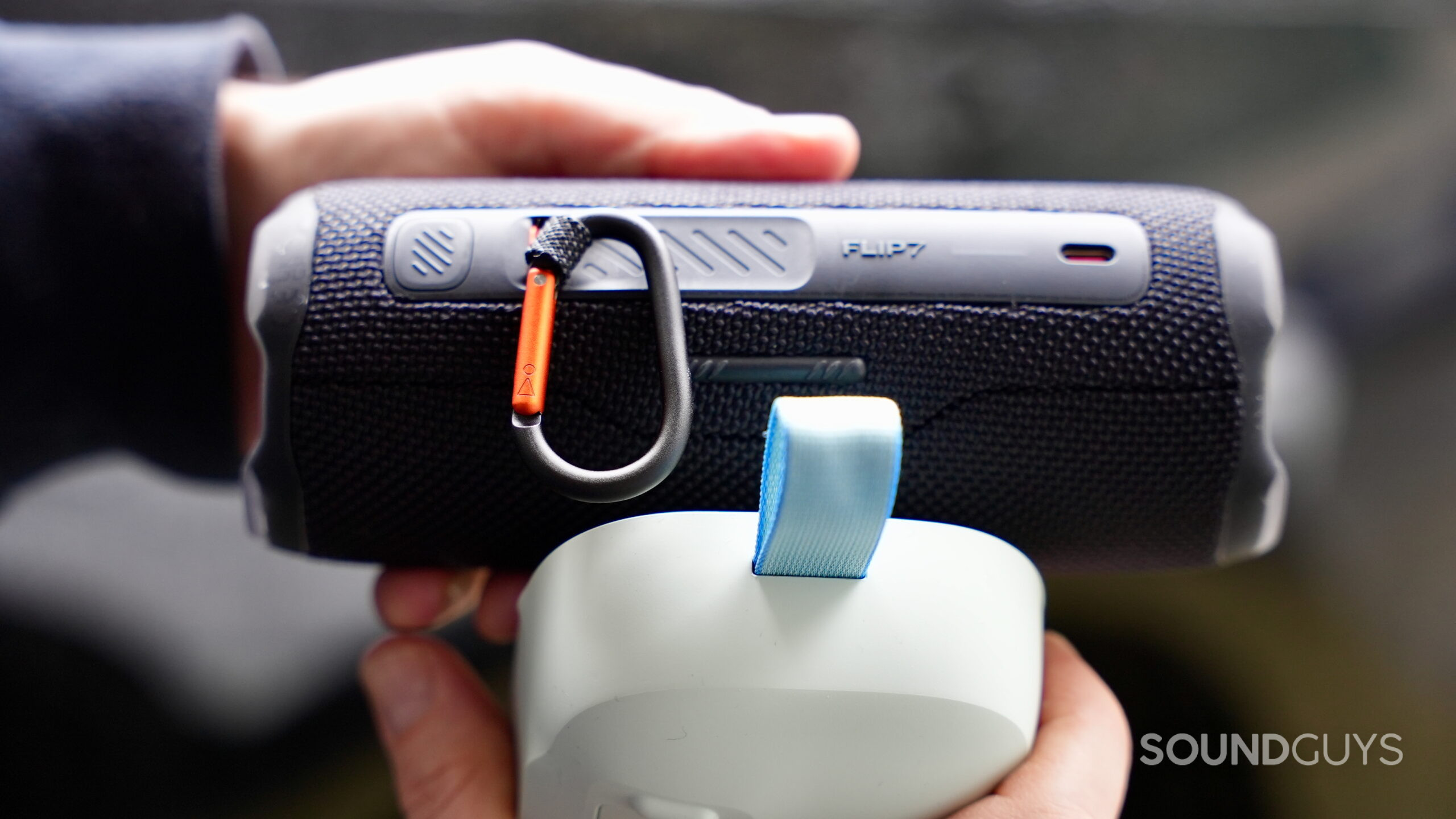 Flip 7 vs Flex 2 - 6 Hands holding the JBL Flip 7 and the Bose SoundLink Flex 2nd Gen, showing their carrying attachments.