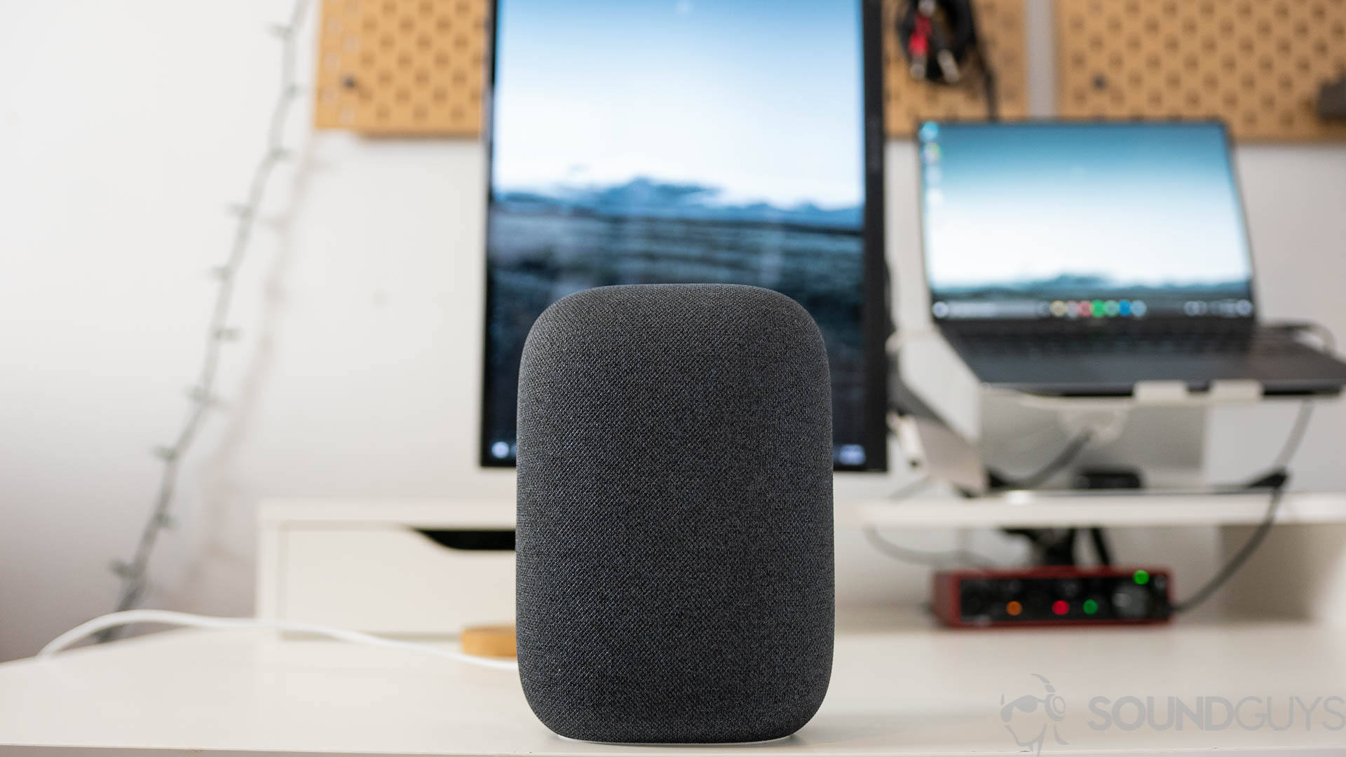 Google Nest Audio from the front The gray Google Nest Audio speaker pictured on a white desk in front of computer screens.