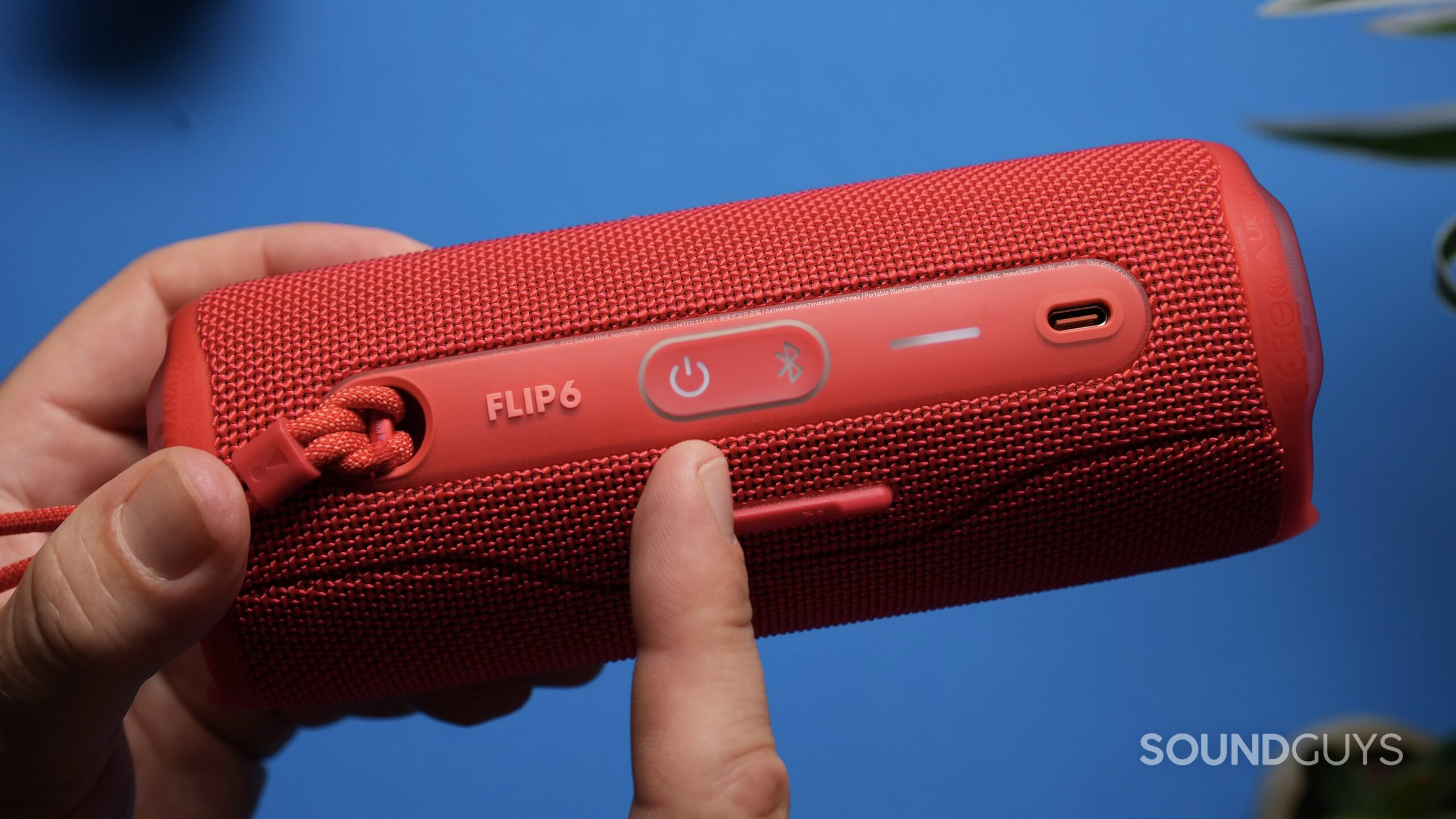 JBL Flip 6 Power button A finger points to the power button on a red JBL Flip 6