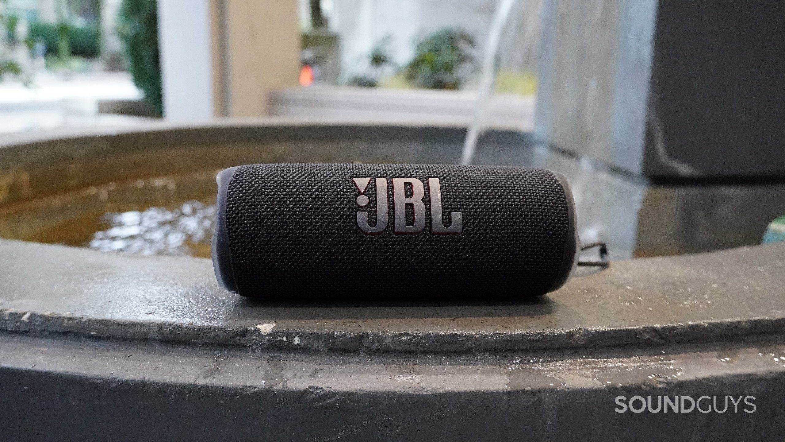 JBL Flip 6 Speaker Outdoor By Fountain A JBL Flip 6 Bluetooth speaker sitting next to a small fountain.